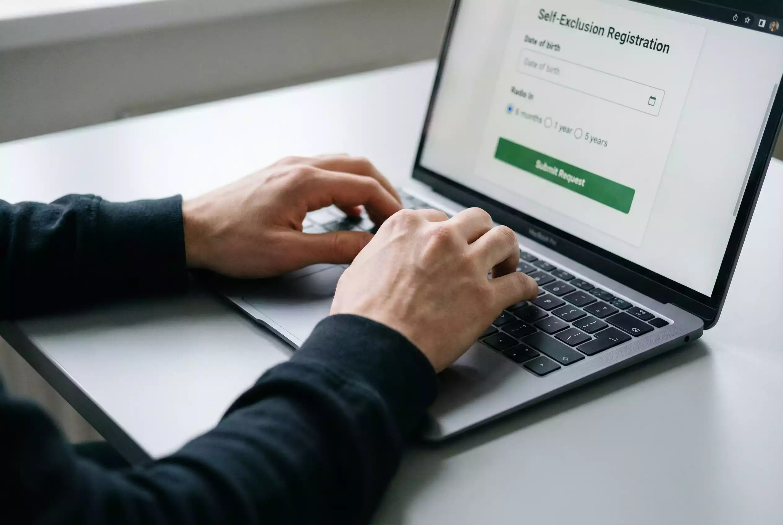Close-up of a person's hands typing on a laptop keyboard with the screen showing a blurred registration form