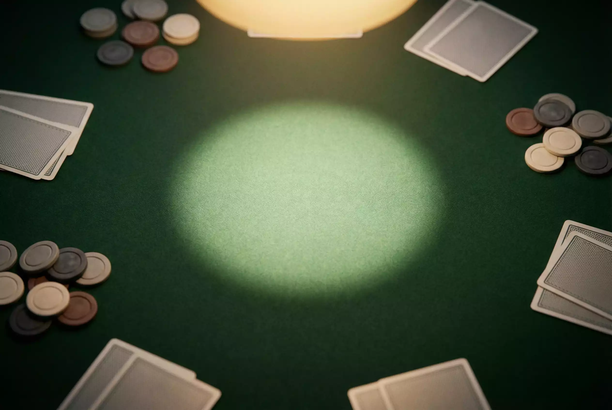Green casino felt table surface under dramatic overhead lighting with scattered playing cards and chips at the edge of frame